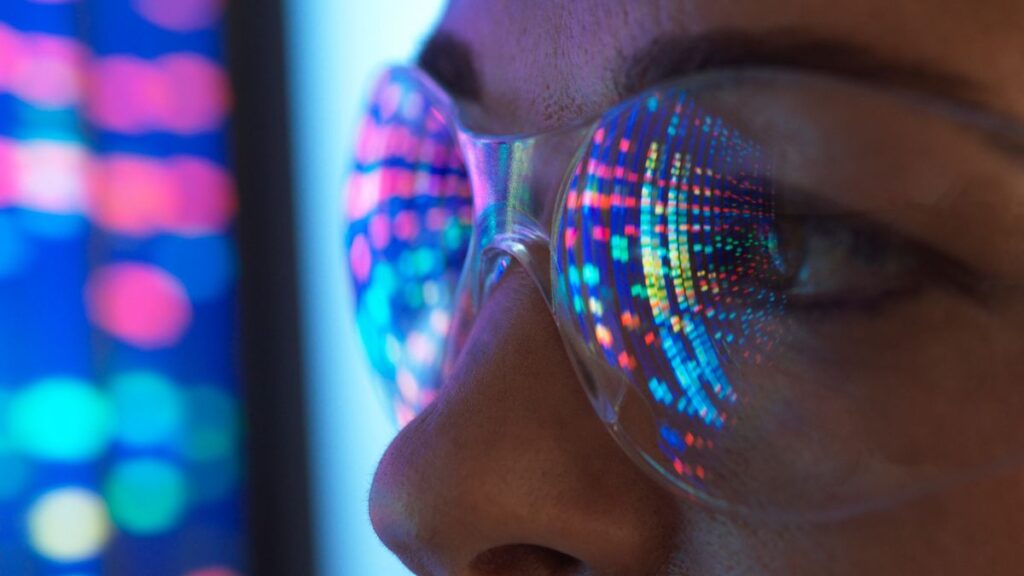 Close-up of scientist with DNA sequencing reflected in eyeglasses.