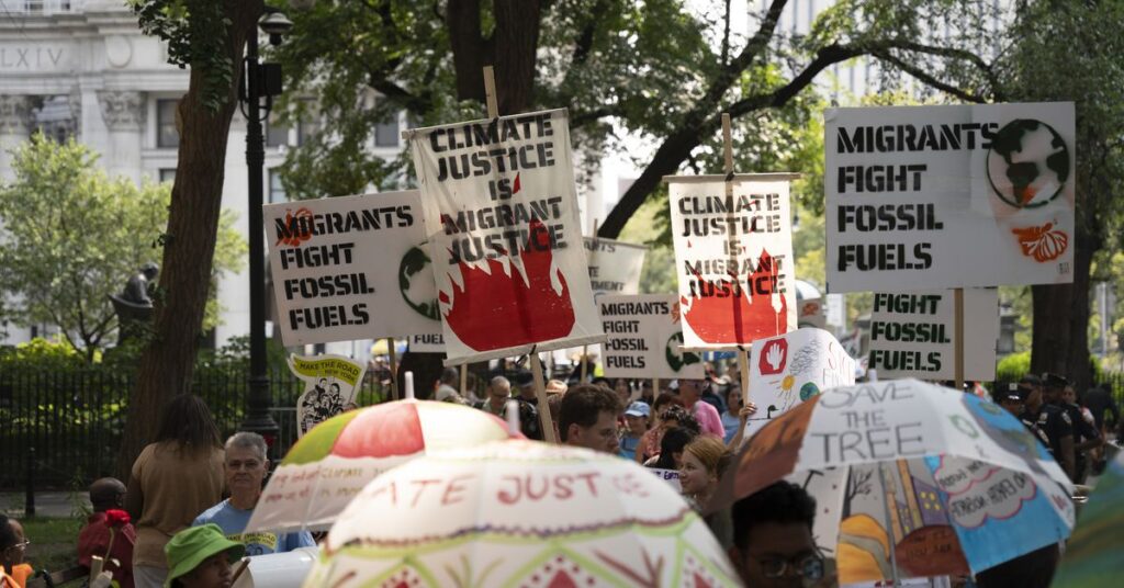 A crowd gathers with people carrying signs that say “climate justice is migrant justice” and “migrants fight fossil fuels.”