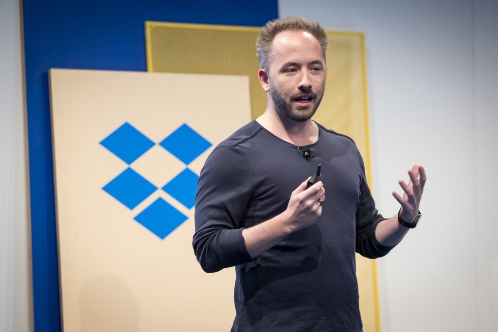 Dropbox CEO Drew Houston speaking with a company logo behind him.