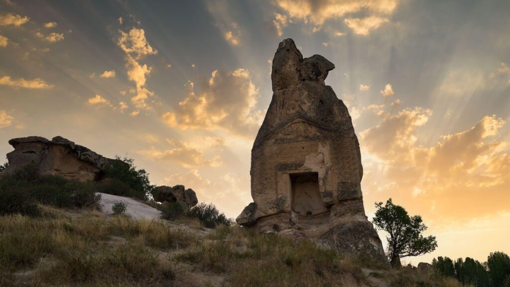 A picture of a stone temple with rays of sun shining behind it