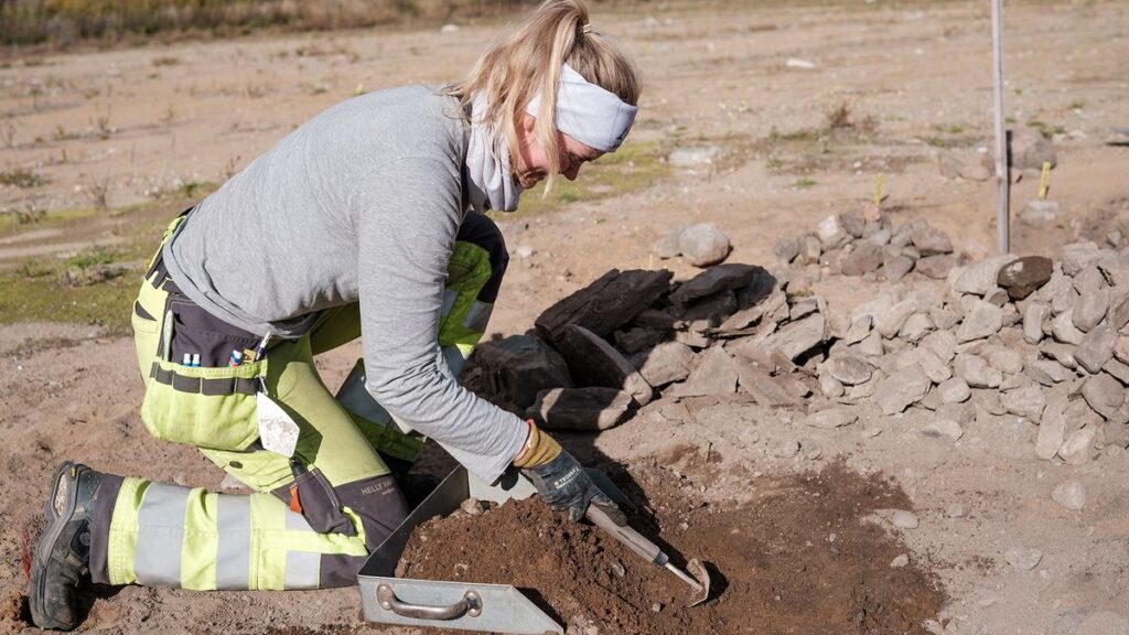 A woman excavates a grave site on rocky soil.