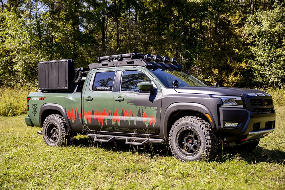 Right profile view of green 2025 Project Trailgater Nissan Frontier parked on grass with trees behind.