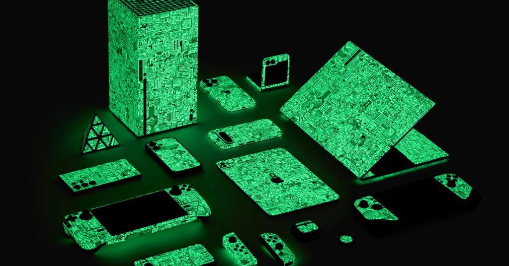 Several different gadgets and gaming devices covered in Dbrand’s Circuit Board wraps and glowing green in the dark.