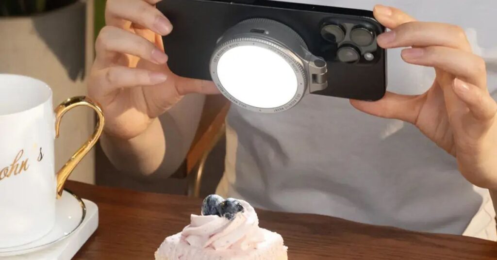 The Harlowe Sol 5 Bi-Color Mobile Light for MagSafe attached to the back of an iPhone photographing a slice of cake.