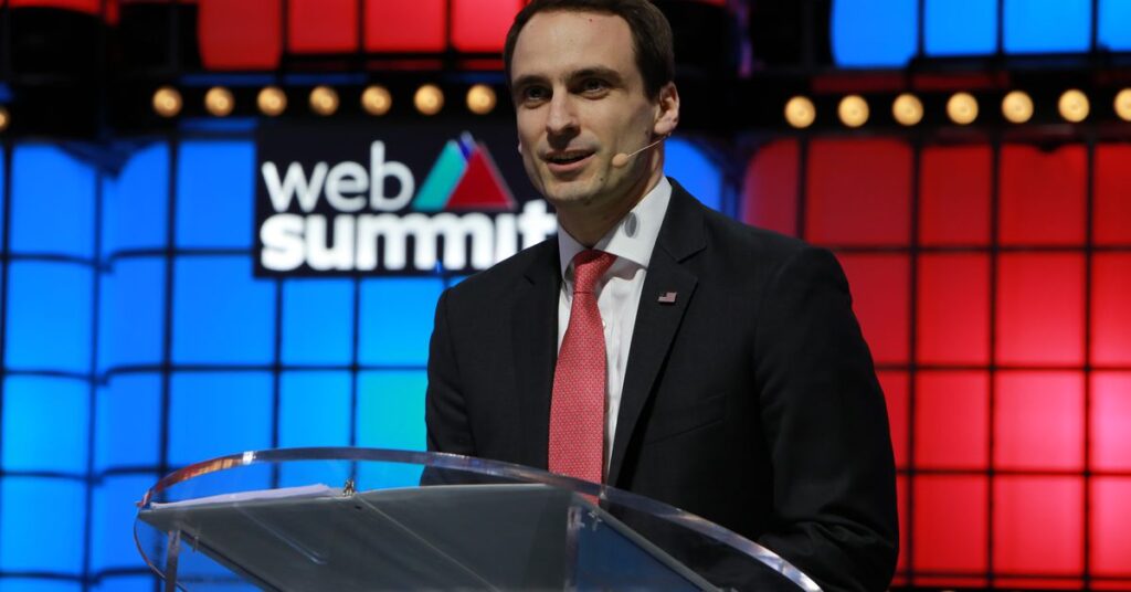 Kratsios standing at a podium with the Web Summit logo on a colorful wall behind him.