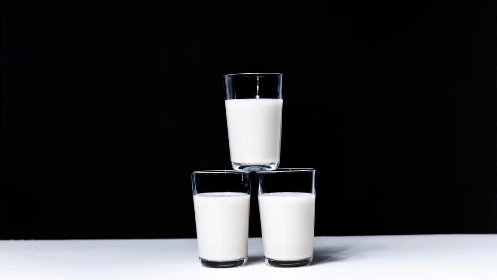 Three glasses of milk on a white table, black background