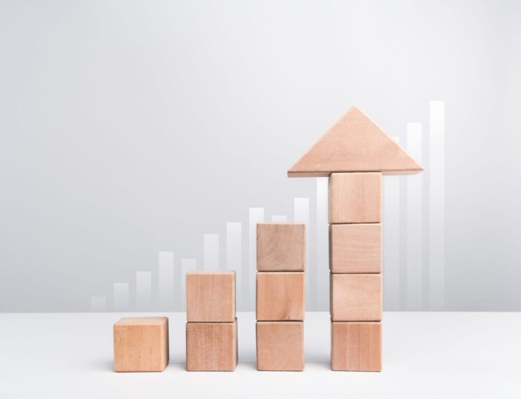 Wooden blocks stacking as an arrow up averages as a growth graph chart on white background.