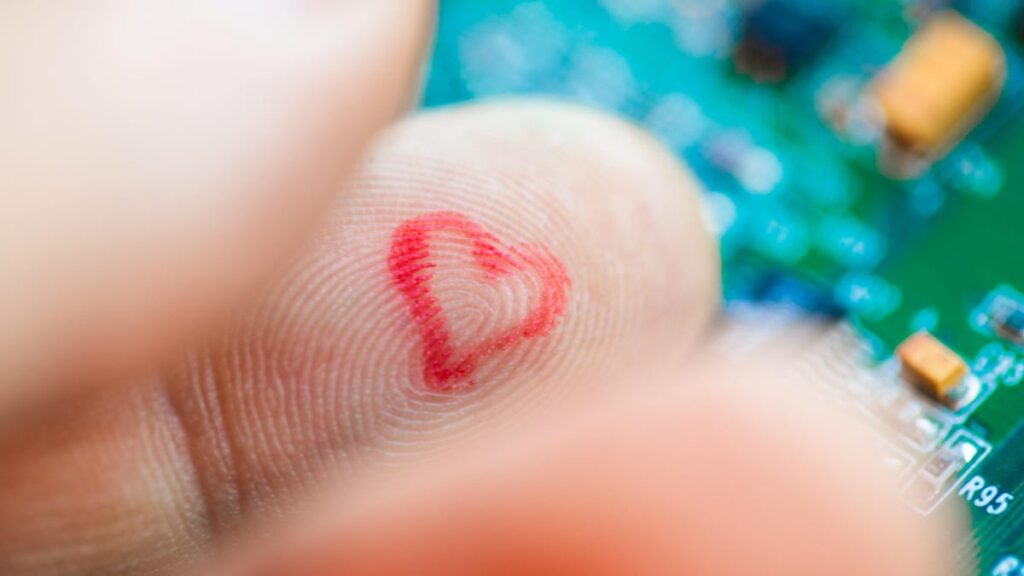 A finger over a circuit board with a small red heart drawn on the finger.