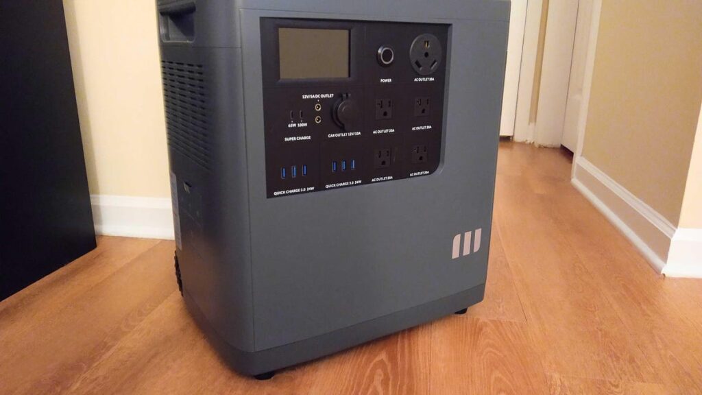 A dark gray portable power station, about a foot and a half tall, sits on a wooden floor.