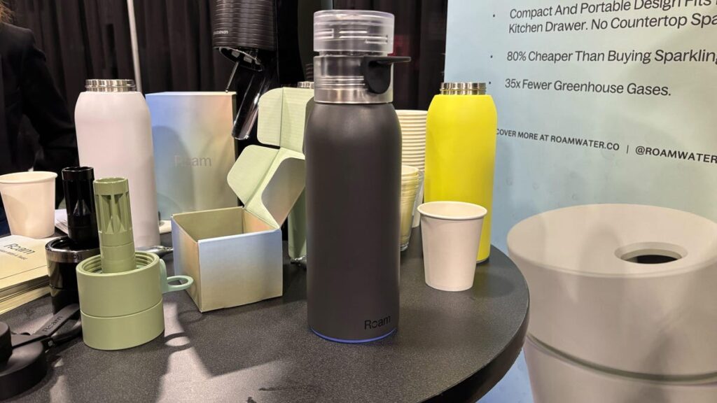 A black stainless steel water bottle sits on a table with cups.